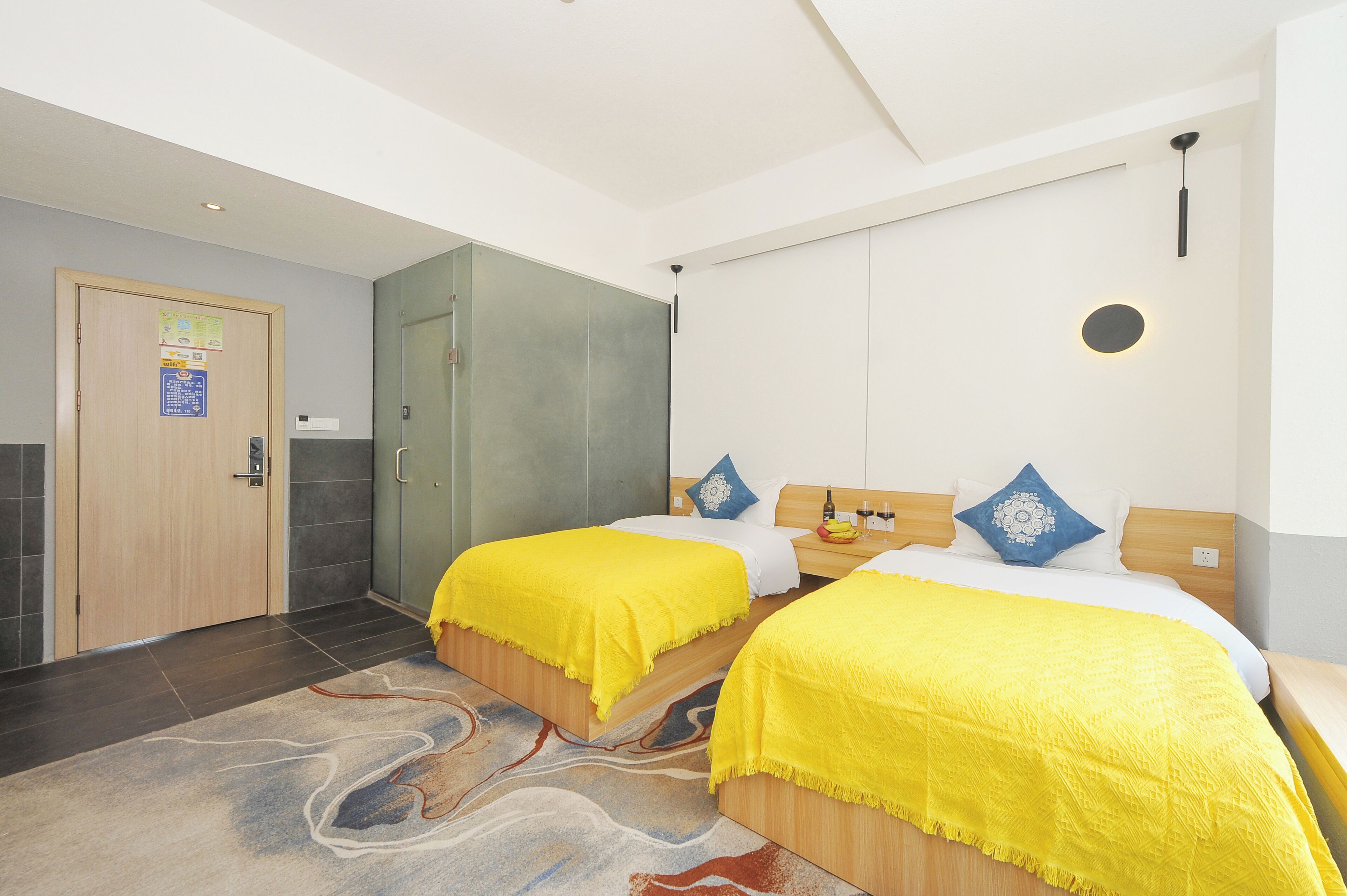 Ett hotellrum med två sängar, en trädörr, en duschkabin med glasväggar och en mönstrad matta.