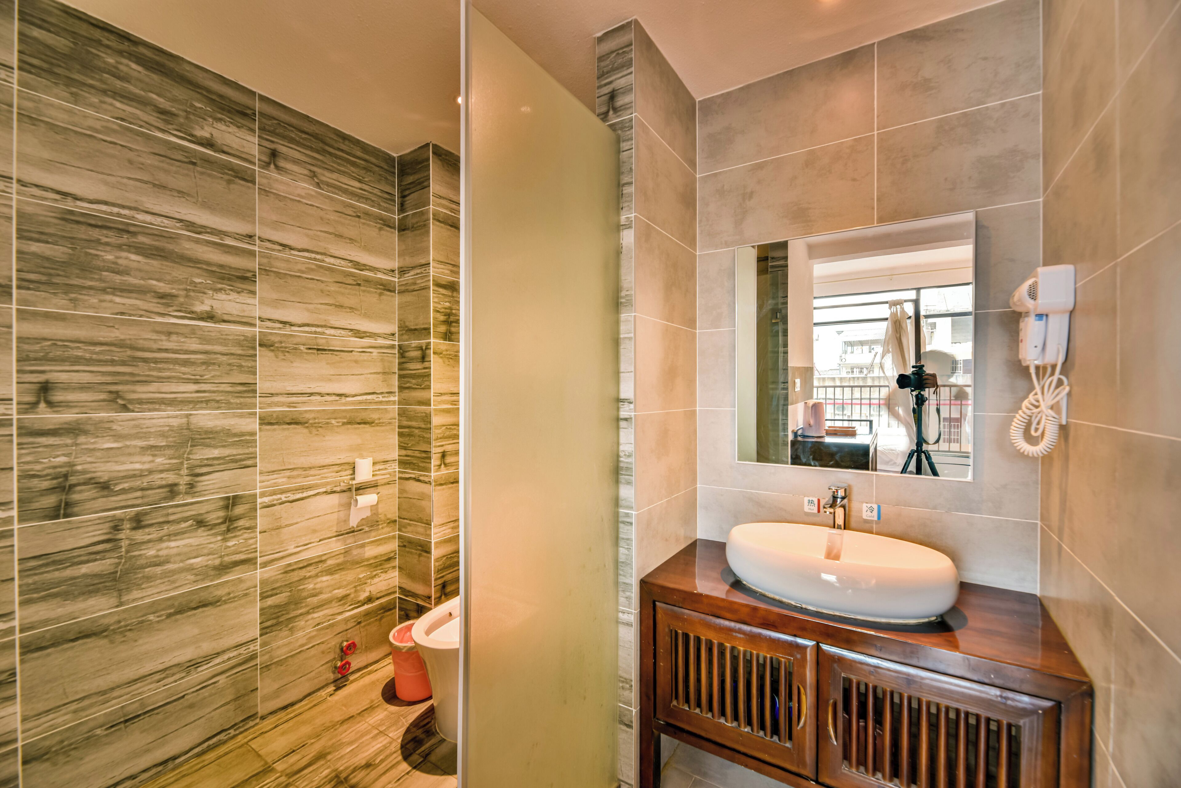 A modern bathroom with a marble wall, a wooden vanity, and a large mirror.