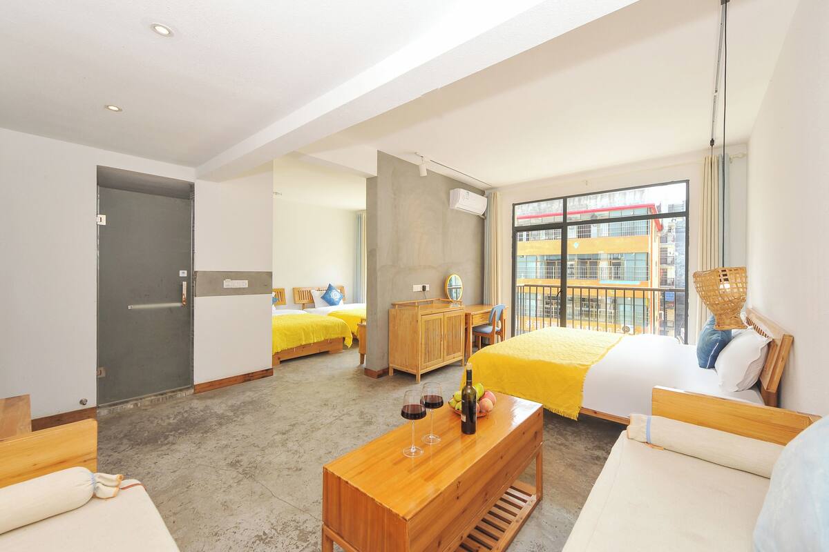 Quarto de hotel com duas camas, uma escrivaninha de madeira, um banco e uma janela grande com vista para a cidade.
