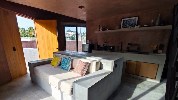 A modern living room with a built-in sofa, a kitchen area, and a large window providing a view of the outside. - Ideal cottage to rest with the family very close to the sea, one pet is accepted. (El Sargento)