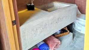 A bathroom with a large, round mirror, a stone sink, and a shelf with towels. - Ideal cottage to rest with the family very close to the sea, one pet is accepted. (El Sargento)