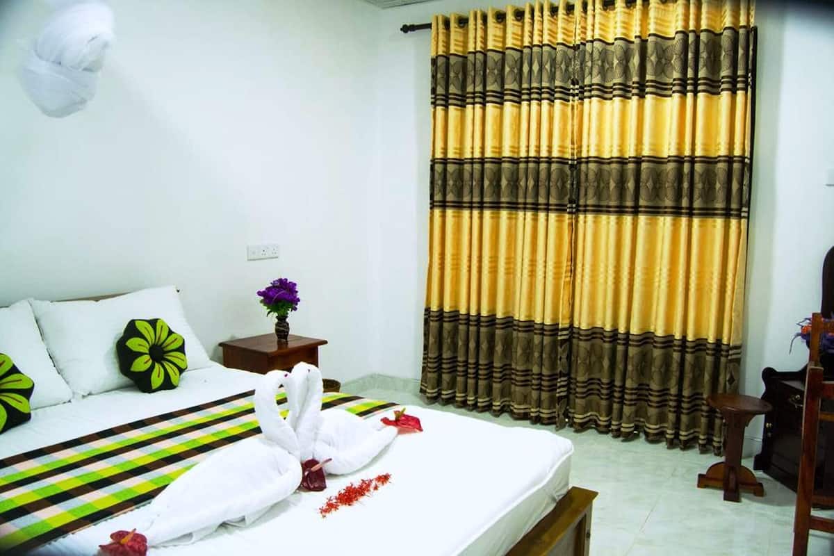A hotel room with a bed, a nightstand, a curtain, and a wall-mounted light fixture.