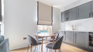 Cozinha moderna com armários cinza, bancada branca e mesa de jantar de madeira com quatro cadeiras.