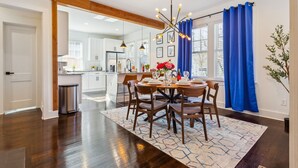 Une cuisine moderne avec des meubles blancs, un coin repas doté d’une table ronde et de chaises, et un rideau bleu.