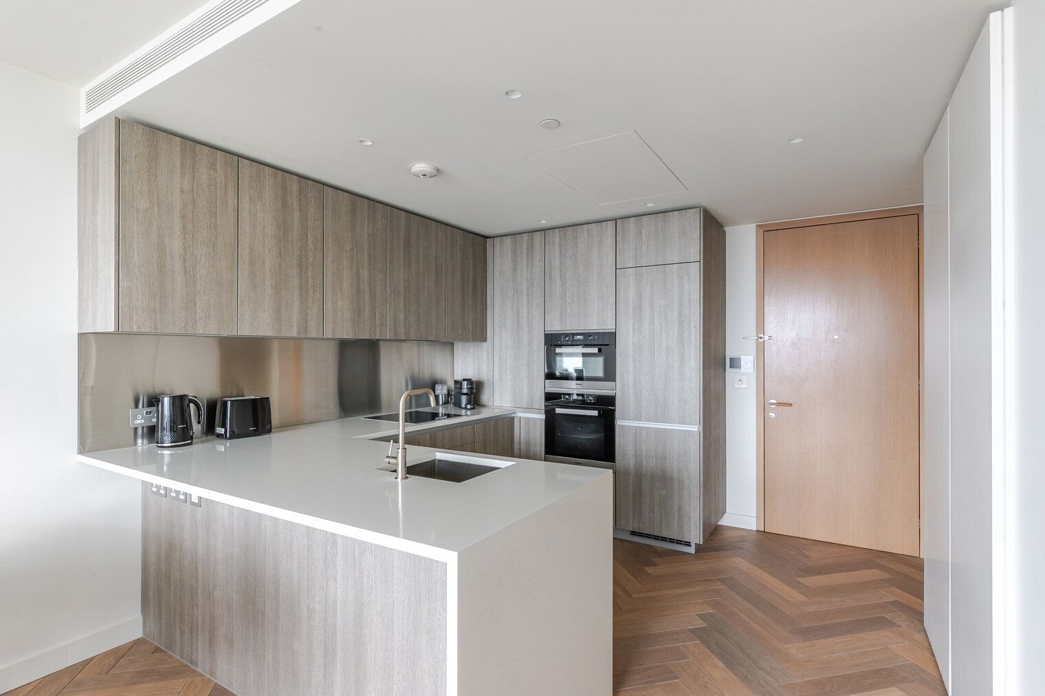 A modern kitchen with a central island, built-in appliances, and a herringbone wood floor.