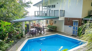 A swimming pool with a covered patio area, surrounded by lush greenery and a two-story building with a balcony. - Brisas de Ballena with Panoramic Ocean View (Uvita)