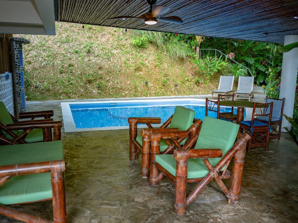 Un espace aménagé au bord de la piscine, avec des chaises en bambou, une table et un ventilateur de plafond.