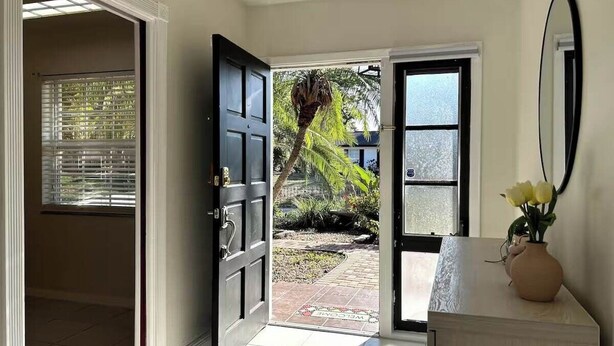 A hallway leading to a door with a view of a garden and a palm tree.