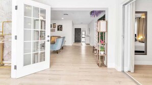 A spacious hallway with a wooden floor, a blue armchair, and a white door with glass panels.
