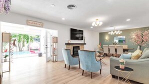 A spacious living room with a fireplace, a television mounted above it, and a dining area with a table and chairs.