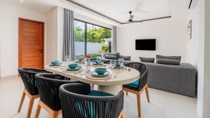 Ein moderner Essbereich mit einem runden Tisch, schwarzen Flechtstühlen und einem grauen Sofa.
