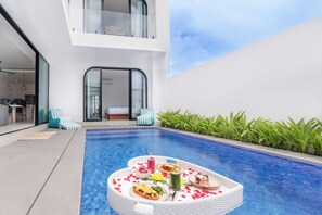Un espace piscine extérieur moderne, aménagé avec un coin repas comprenant une table, des chaises et une variété de plats et de boissons.