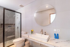 Une salle de bain moderne avec une douche à parois de verre, un lavabo blanc et un miroir rond.