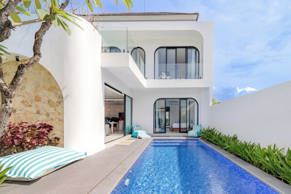 Une maison moderne à deux étages, dotée d’une piscine, de portes vitrées et d’un mur en pierre.