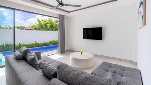 Ein modernes Wohnzimmer mit einer grauen Eckcouch, einem runden Couchtisch und einem an der Wand befestigten Flachbildfernseher.
