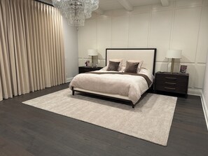 Ein modernes Schlafzimmer mit einem großen Bett, dunklem Holzboden, beigefarbenen Vorhängen und einem Kronleuchter.