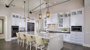 A modern kitchen with white cabinetry, a central island with bar stools, stainless steel appliances, and pendant lighting.