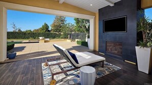A modern outdoor living area with a lounge chair, a fireplace, and a TV mounted on the wall.