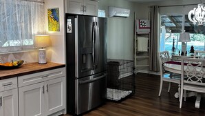 Uma cozinha moderna com geladeira de aço inoxidável, uma área de jantar com mesa e cadeiras brancas e um lustre no teto.