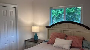 Um quarto com cama, janela, abajur e porta.