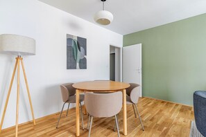 Een moderne woonkamer met een ronde houten tafel, vier beige stoelen, een vloerlamp en abstracte kunst aan de muur.