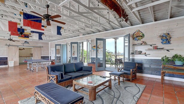 A spacious living area with a high ceiling, a ping pong table, comfortable seating, and a large window offering a view of the outdoors.