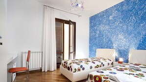 A hotel room with two beds, a chair, a radiator, a window with curtains, and a blue textured wall. - Beautiful private villa for 6 people with A/C, WIFI, private pool, TV, veranda and panoramic view (Cornino)