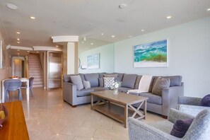 A modern living room with a grey sofa set, a wooden coffee table, and a painting of a seascape on the wall. - 3 Ocean Front Units * 3 Patios * 2 Levels (San Diego)