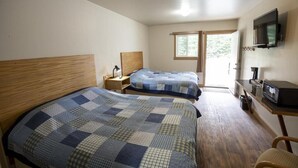 A bedroom with two beds, a wooden headboard, a nightstand, a TV, and a window. - Tatogga Lake Resort (Iskut)