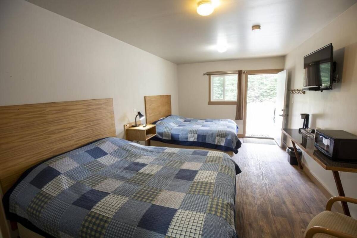 A bedroom with two beds, a wooden headboard, a nightstand, a TV, and a window.