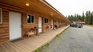 A row of log cabin-style rooms with a covered outdoor seating area and a gravel driveway. - Tatogga Lake Resort (Iskut)