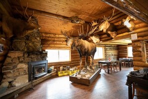 A log cabin interior with a stone fireplace, wooden dining area, and mounted animal heads. - Tatogga Lake Resort (Iskut)