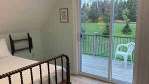 Quarto com cama de madeira, ventilador de teto e vista para um deck e jardim através de uma porta de correr de vidro.