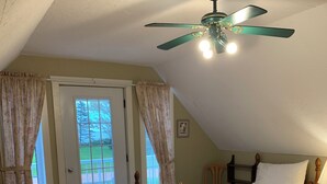 Quarto com duas camas de madeira, um ventilador de teto e uma porta que dá para uma área externa.