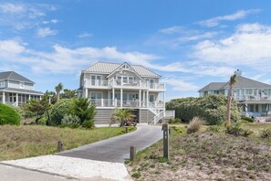 Ein Strandgrundstück mit einem großen Haus, das einen Balkon, einen überdachten Gang und einen Sandstrand bietet.