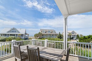 Une terrasse en bois avec une table et des chaises, des rampes blanches et des maisons en arrière-plan.