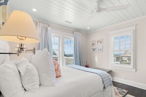 Ein Schlafzimmer mit Bett, Deckenventilator, Fenster mit Jalousien und Meerblick.