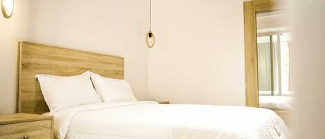 A neatly made bed with a wooden headboard, a bedside table with a drawer, and two pendant lights.