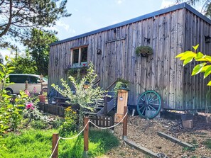 A rustic wooden building with a porch, a wheelbarrow, and a garden with various plants and flowers. - Tiny House Cottage Herbert by Interhome (Grossschönau)