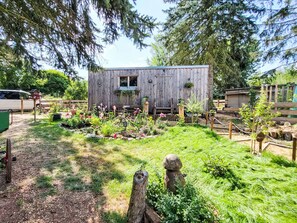 A wooden cabin with a small window, surrounded by a garden with various plants and a wooden fence. - Tiny House Cottage Herbert by Interhome (Grossschönau)