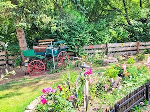 Um jardim com um carrinho antigo, cerca de madeira e diversas plantas.