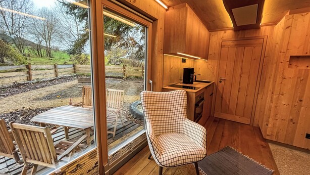 Ein Holzinterieur mit Essbereich, einer Küche inklusive Kaffeemaschine und Blick ins Freie.