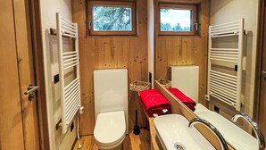 Ein kleines Badezimmer mit Holzwänden, einer Toilette, einem Waschbecken und einem Fenster.