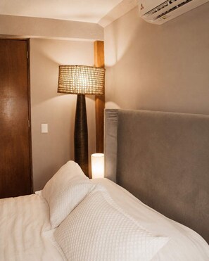 Ein Hotelzimmer mit einem Bett, einem Nachttisch, einer Lampe und einer Klimaanlage.