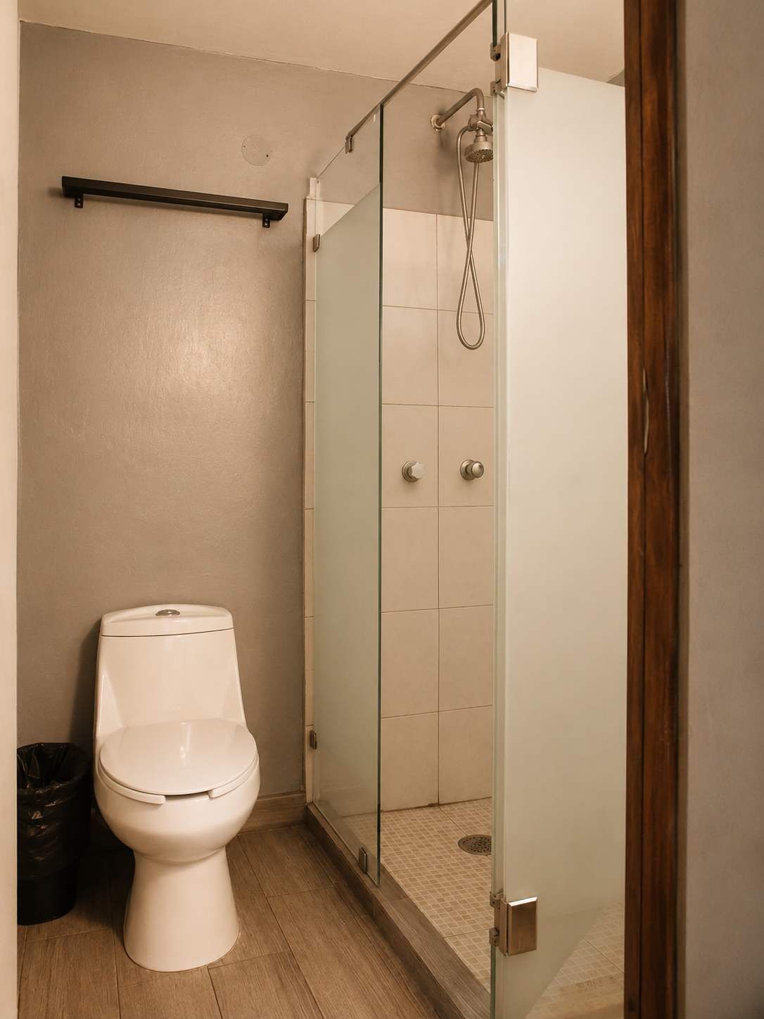 Une salle de bain avec des toilettes, une douche à parois de verre et un plancher en bois.