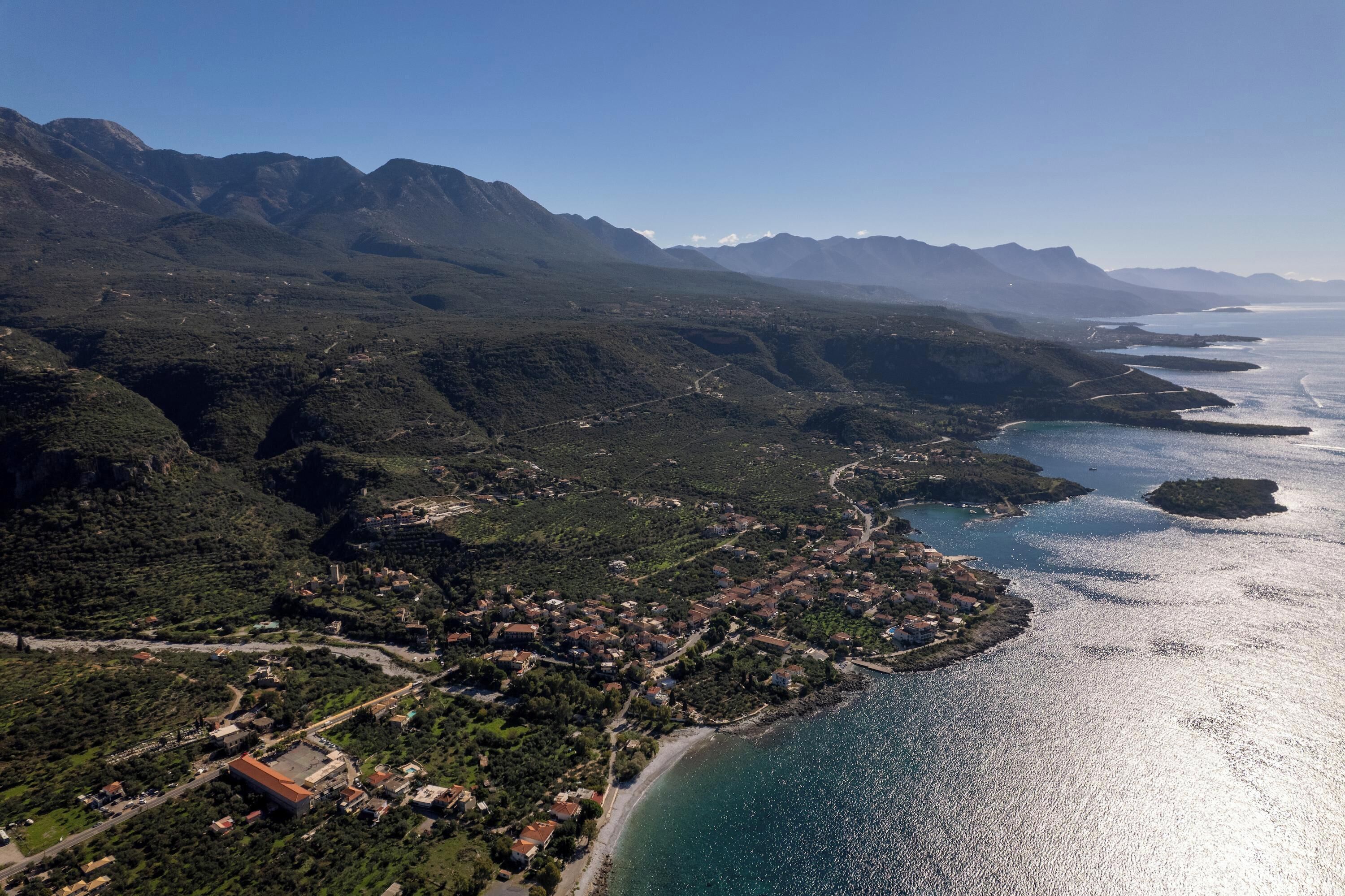 An aerial view of a coastal town with mountainous terrain, a beach, and a clear sky.