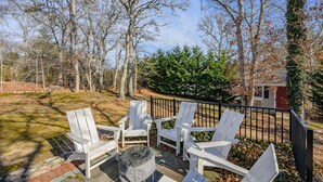 Eine Terrasse mit vier weißen Adirondack-Stühlen und einem Steinkamin, umgeben von einem schwarzen Metallzaun.