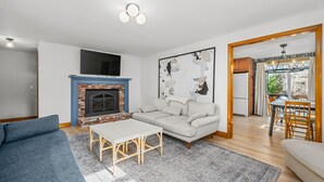 Ein Wohnzimmer mit Kamin, einer Couch, einem Couchtisch und einem an der Wand montierten Fernseher.