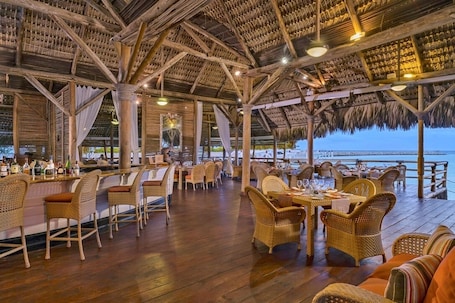 An outdoor restaurant with wooden furniture and a thatched roof, overlooking a beach.. Corales 50 - Golf front villa with ocean view with full staff
