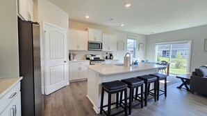 A modern kitchen with white cabinetry, a central island with stools, a microwave, and a stove. - New 2025 Beach Home! Ocean View Beach Club! 5 Minutes to Bethany Beach (Ocean View)